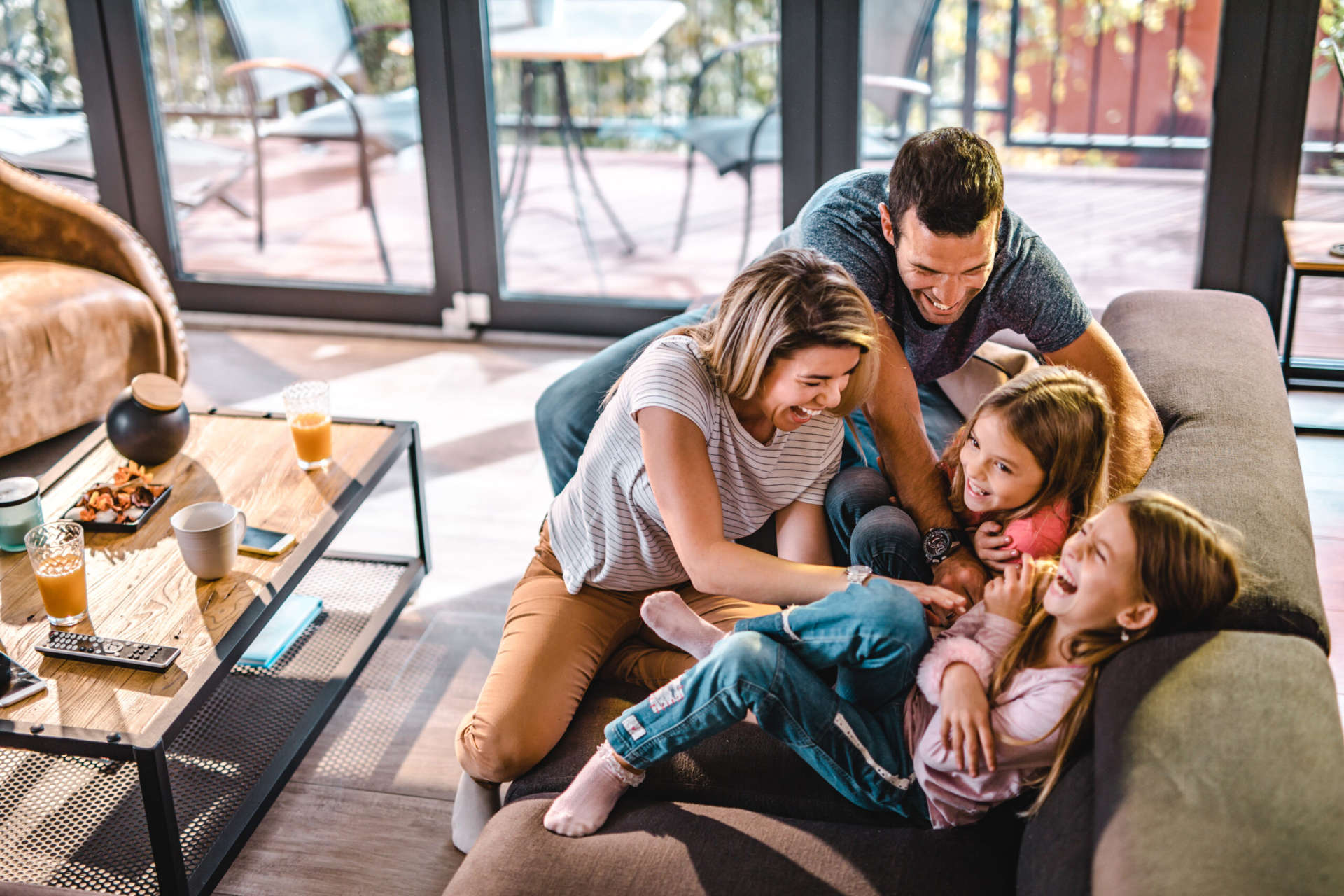 High angle view of cheerful parents having fun while tickling their daughters on sofa in the living room.